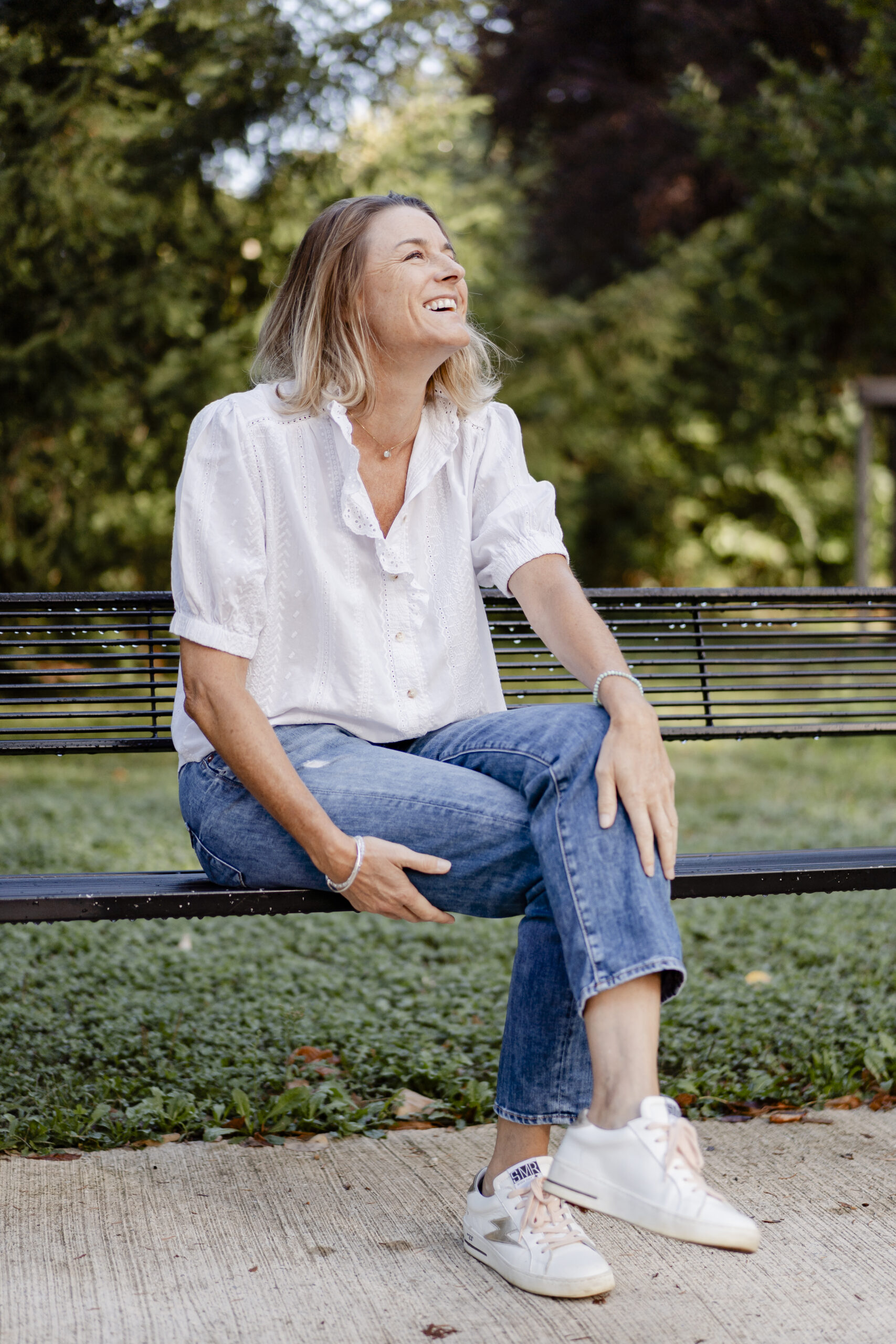 Portrait de la praticienne assise en extérieur, souriante, dans un cadre naturel.